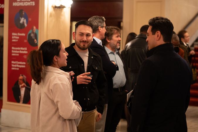 three audience members chat and enjoy drinks in the lobby at intermission