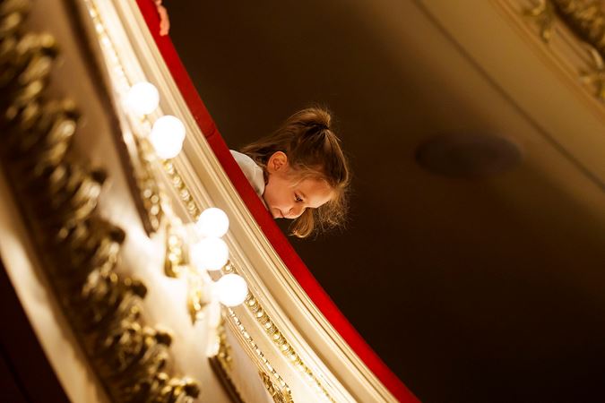 A young female student looking over the Lower Balcony railing at the main floor