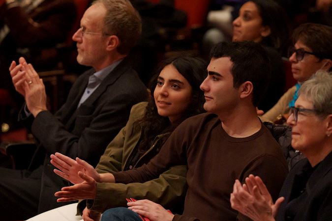 a young couple in the audience uses each other's hands to clap for the performance
