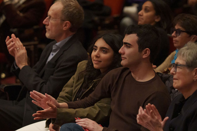a young couple in the audience uses each other's hands to clap for the performance
