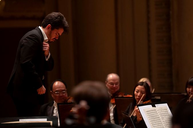 Shani prepares to conduct with his hand across his chest