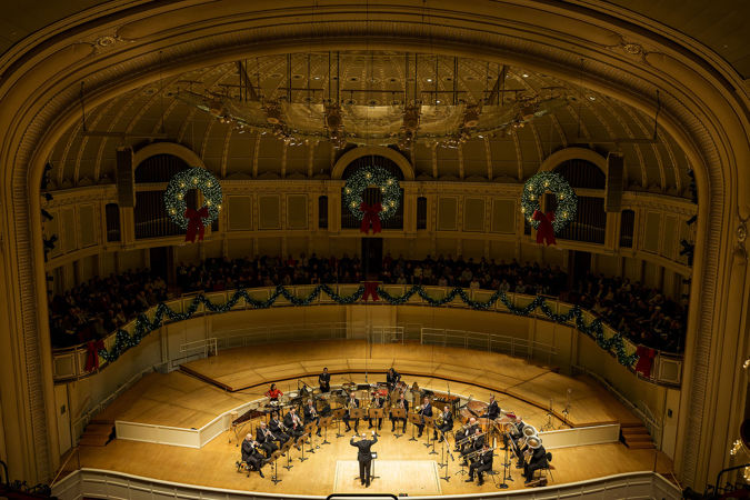 a wide shot of the CSO Brass and Percussion sections on stage in a festively decorated Orchestra Hall