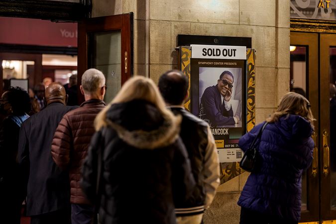 a crowd forms a line outside the doors of Orchestra Hall on Michigan Avenue next to the sold-out poster, waiting to have their tickets scanned