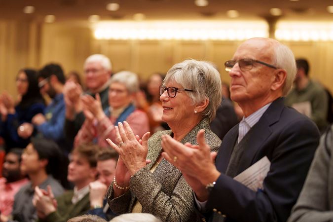 two audience members clap during a standing ovation for the orchestra