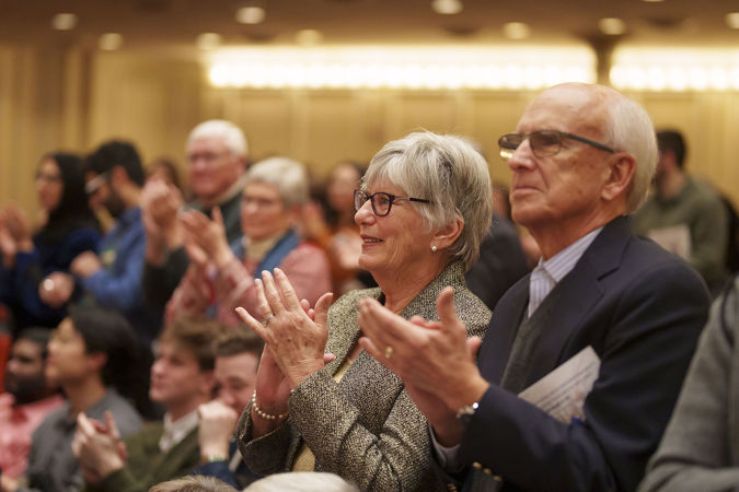 two audience members clap during a standing ovation for the orchestra