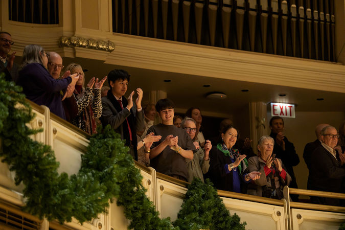 audience members in the terrace, amid festive garland in the hall for the holiday season, give the orchestra a standing ovation