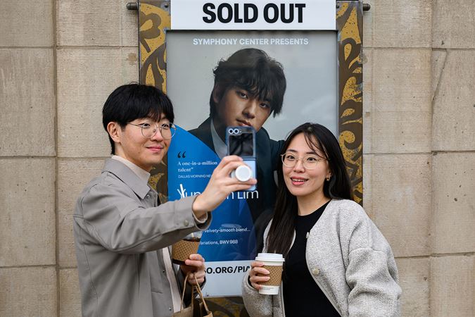 two young fans smile and take a selfie together in front of the sold out concert poster