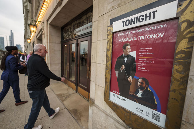 eager audience members enter Orchestra Hall next to the evening's concert poster