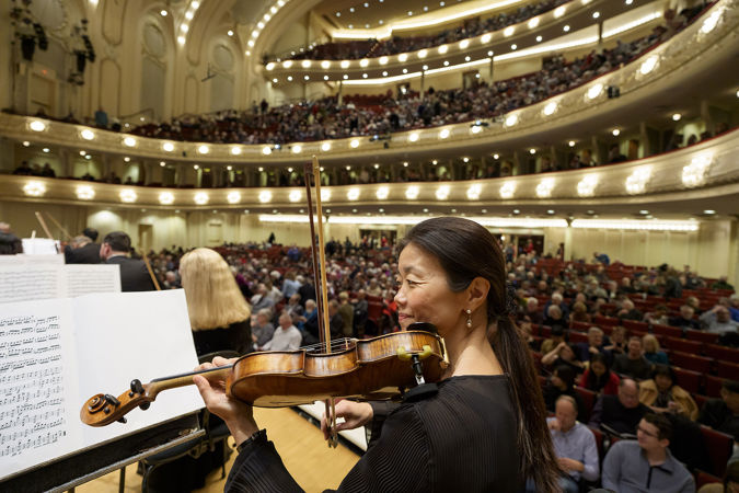 CSO violinist Qing Hou warms up on stage, the audience filing into the hall behind her