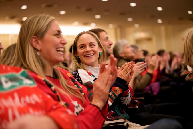 Closeup of two concert attendees in festive sweaters applauding