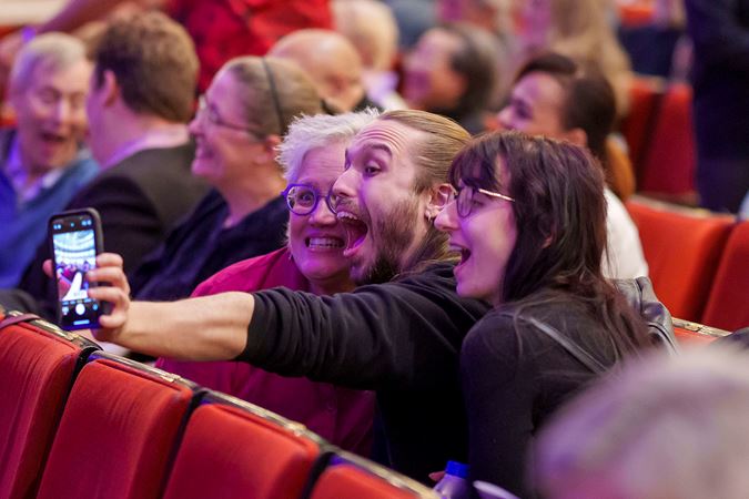 three excited audiences members take a selfie from their seats before the show