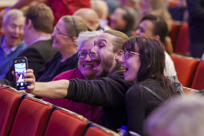 three excited audiences members take a selfie from their seats before the show