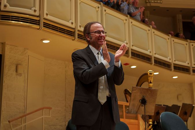 composer Christopher Theofanidis applauds the Orchestra from the side of the stage