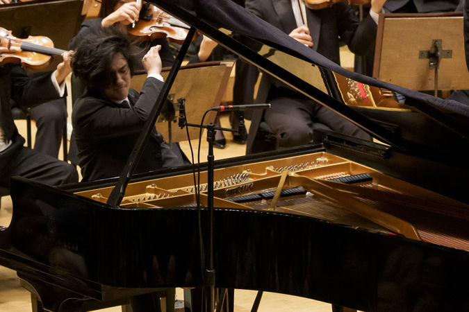 Yunchan Lim, seen through the window of the piano, raises his right arm in a final flourish
