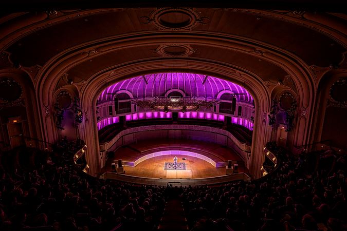 a bird's eye view of Chris Thile in recital as the audience in the balcony watches intently