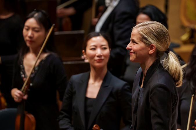 members of the CSO violin section look on as Karina Canellakis smiles at the audience and prepares for a postconcert bow