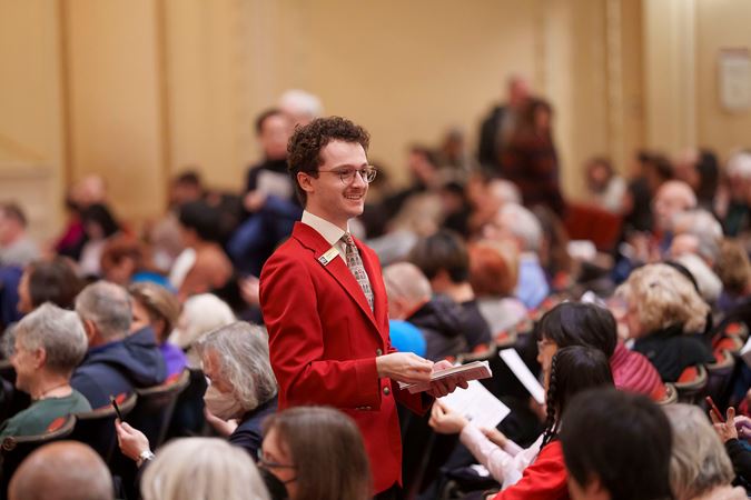 An usher walking down the Main Floor aisle handing out programs