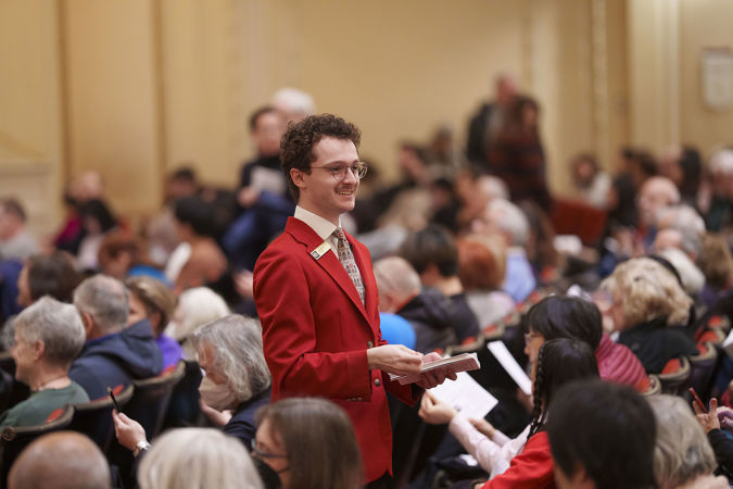 An usher walking down the Main Floor aisle handing out programs
