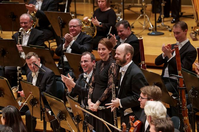 English horn player Scott Hostetler takes a solo bow while his fellow woodwind section members smile and cheer him on
