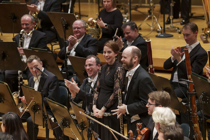 English horn player Scott Hostetler takes a solo bow while his fellow woodwind section members smile and cheer him on
