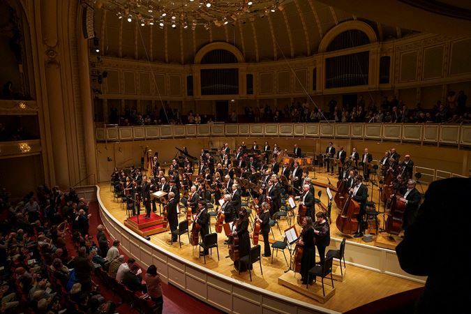 a point of view from the right side of the box level of the Orchestra and Karina Canellakis bowing together