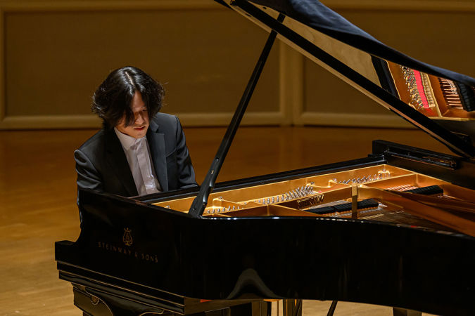 a point of view through the open piano lid as Yunchan Lim concentrates on playing a passage of Bach