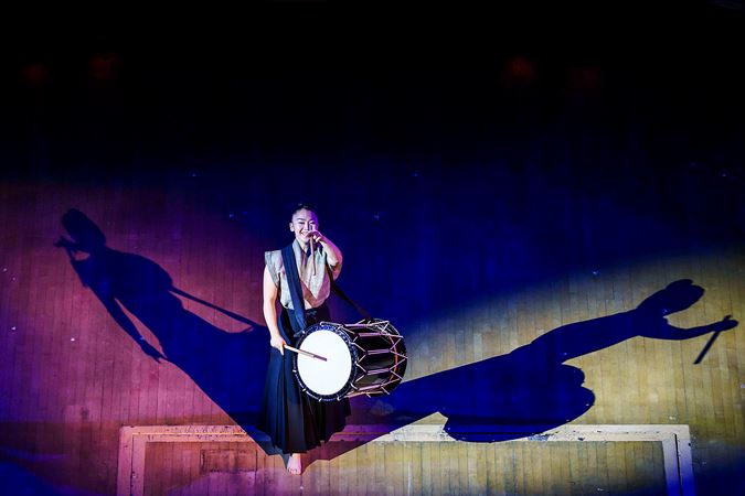 a Kodo member raises her drumstick to the sky mid-performance