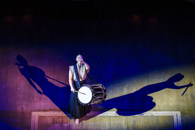 a Kodo member raises her drumstick to the sky mid-performance