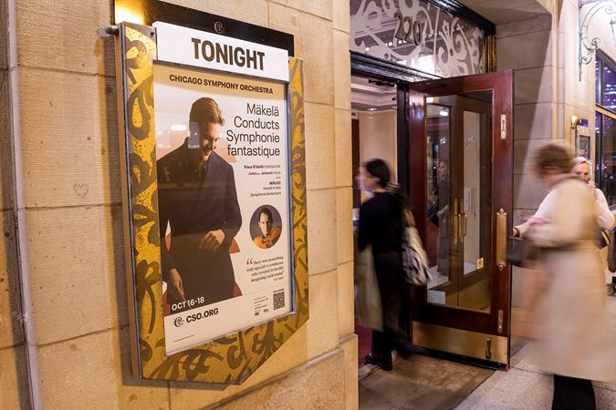 audience members enter the hall on Michigan Avenue next to the concert poster, featuring a photo of Klaus Mäkelä