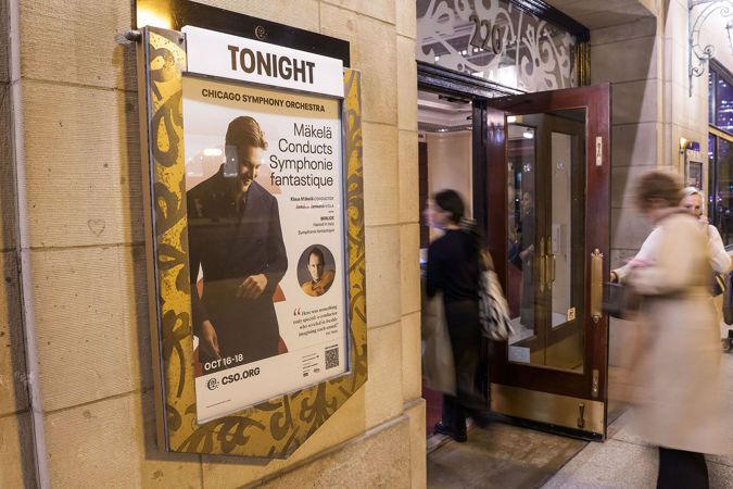 audience members enter the hall on Michigan Avenue next to the concert poster, featuring a photo of Klaus Mäkelä