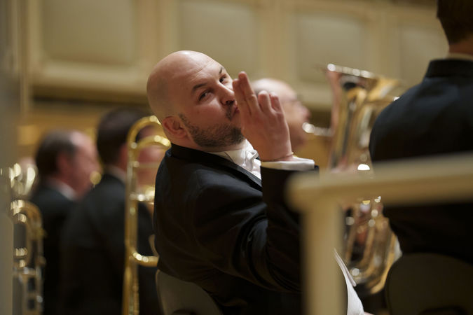 CSO principal trumpet Esteban Batallán lifts his hand in greeting and makes a face at the camera during warm-ups