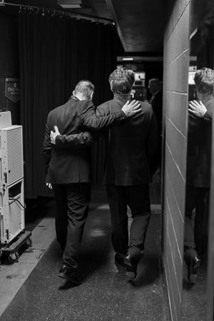 Jakub Hrůša and Simon Trpčeski walk arm in arm backstage, in black and white