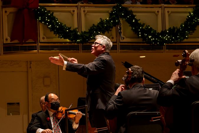 Closeup of John Morris Russell inviting audience members to singalong to a carol
