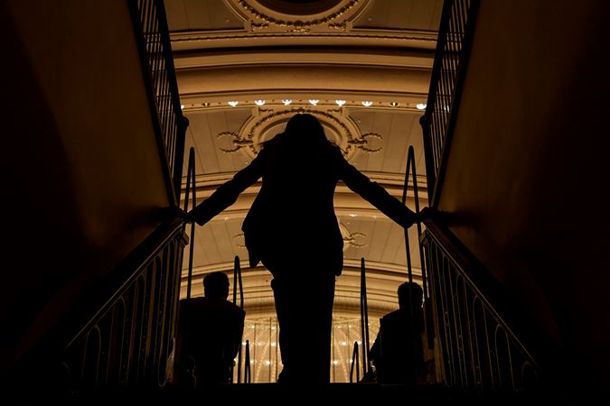 from behind, an usher watches the action unfold in shadow from the steps of the lower balcony