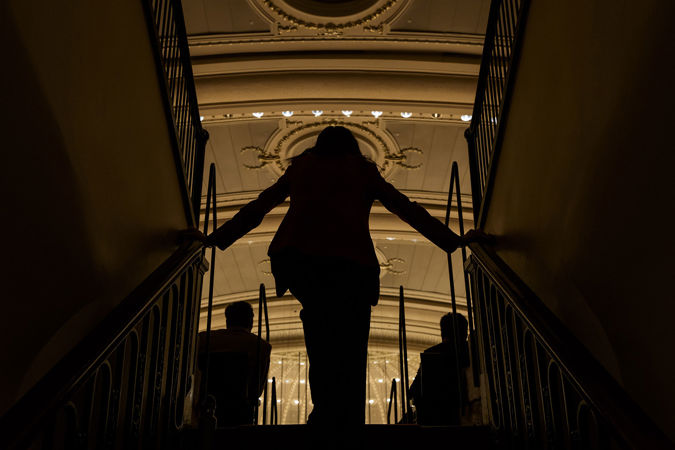 from behind, an usher watches the action unfold in shadow from the steps of the lower balcony