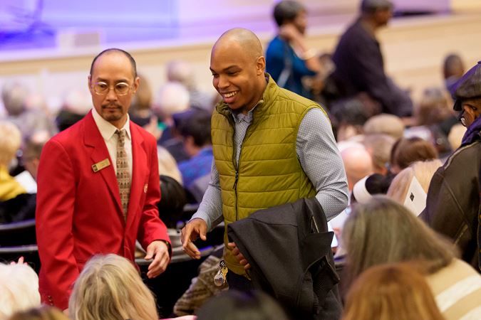 an usher in a red coat directs an excited audience member to his seat on the Main Floor