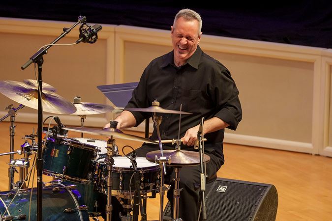 drummer Mauricio Zottarelli closes his eyes and laughs in the middle of performing a joyful piece