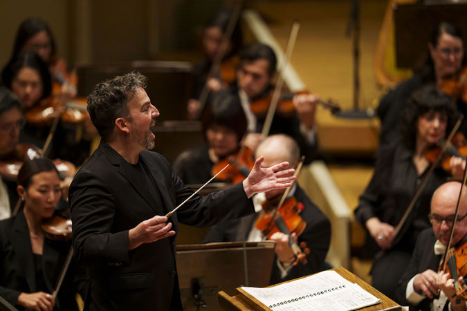 conductor James Gaffigan gives an enthusiastic, open-mouthed smile as he gestures to the Orchestra during a piece