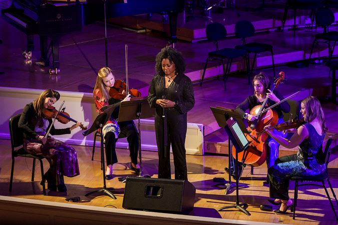 Wide shot of ensemble ATLYS and singer Simbryt Dortch performing a Notes for Peace tribute song