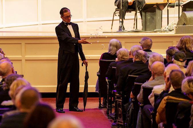 ensemble member Guy Bellingham tosses fake snow on an audience member in the front row