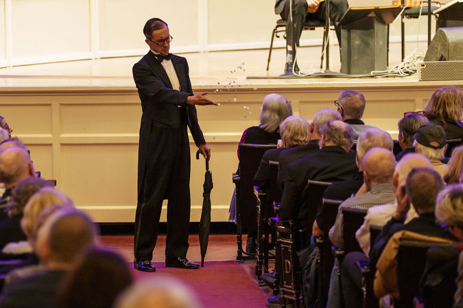 ensemble member Guy Bellingham tosses fake snow on an audience member in the front row