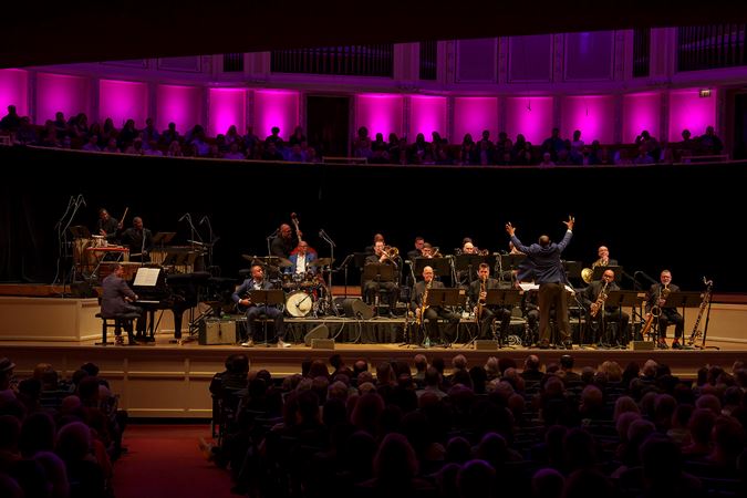 a view of the entire ensemble and guest artists on stage from the back of the main floor, as John Clayton raises both arms for the final cue