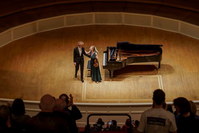 Violinist Julia Fischer and pianist Jan Lisiecki smiling at each other before they bow