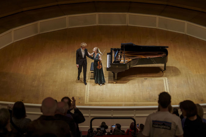 Violinist Julia Fischer and pianist Jan Lisiecki smiling at each other before they bow