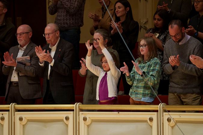 a group of audience members ranging from young to old finds common ground in the music as they rise in a standing ovation