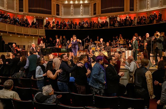 a conga line forms on the main floor of Orchestra Hall as Pink Martini performs