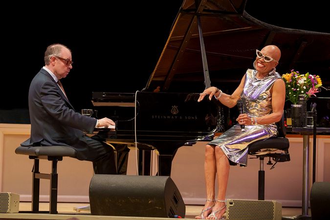 Dee Dee Bridgewater smiles mid-performance with mic in hand, accompanied by Bill Charlap at the keyboard