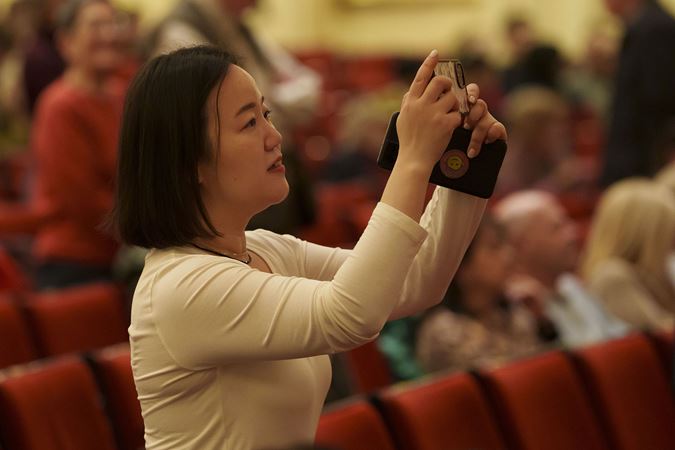 an audience member with dark, shoulder-length hair and a cream-colored top takes a photo on the Main Floor at intermission