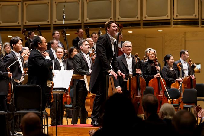 Klaus Mäkelä smiles on the podium, about to take a bow with the Orchestra