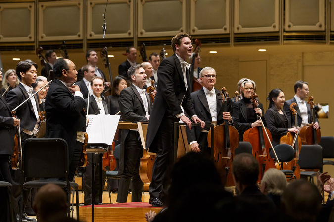 Klaus Mäkelä smiles on the podium, about to take a bow with the Orchestra